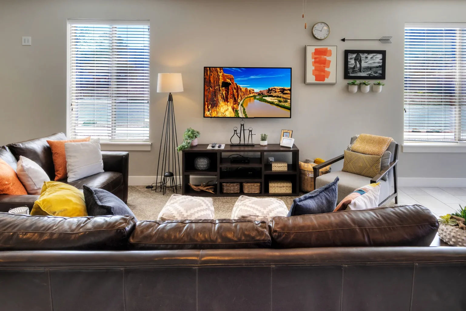 Modern living room with brown leather sectional and canyon landscape on a mounted TV Wall-mounted TV with integrated cable management in Entrada Moab townhome showing scenic canyon landscape photography.