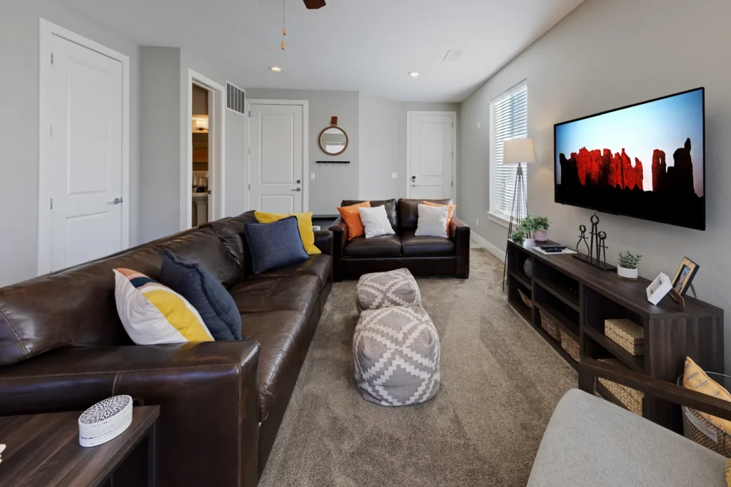 Premium leather sofas and patterned ottomans in the living area of Entrada Moab Townhome 417 with a view of red rock landscape art.
