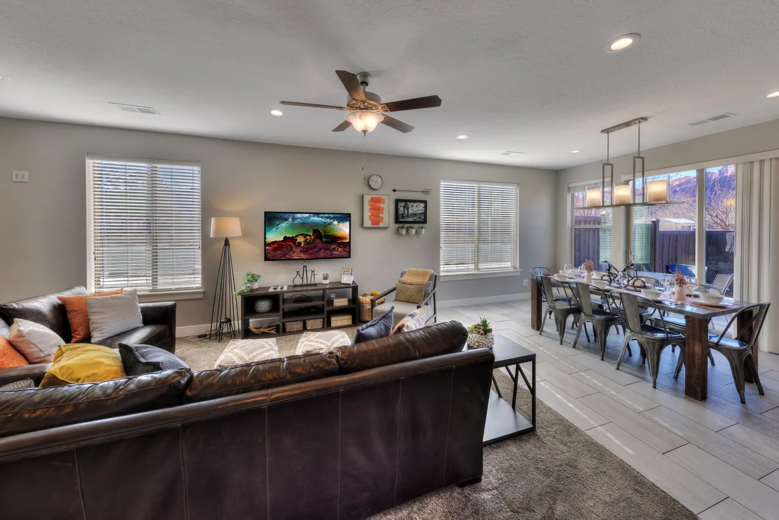 Open-plan living and dining room with gray walls and large windows Dining area in an end-unit Entrada Moab townhome with seating for eight and views of red rock cliffs through the patio door.