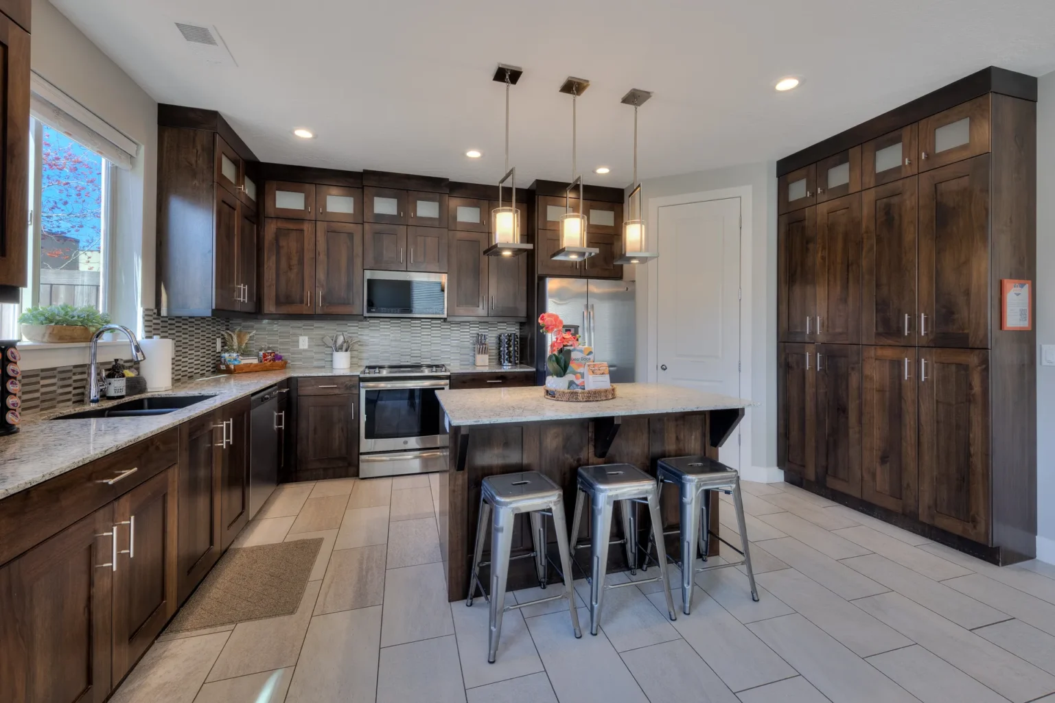 Midnight Wood Kitchen with Glass Tile and Stainless Pendant Island Fully equipped kitchen in Entrada Moab townhome 417 featuring dark cabinetry, granite island, and GE Profile appliances.
