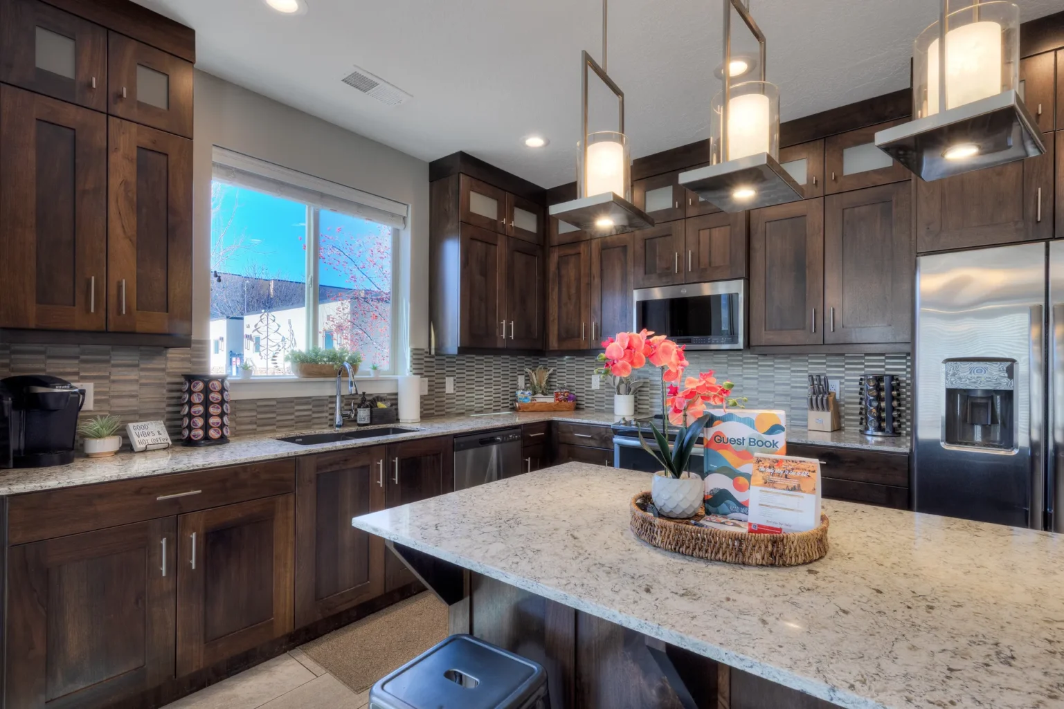 Modern Kitchen Glow: Dark Wood, Light Granite, and Pink Floral Accent Kitchen sink area with a view of Moab red rock cliffs, featuring a dual coffee station with Keurig and drip options.