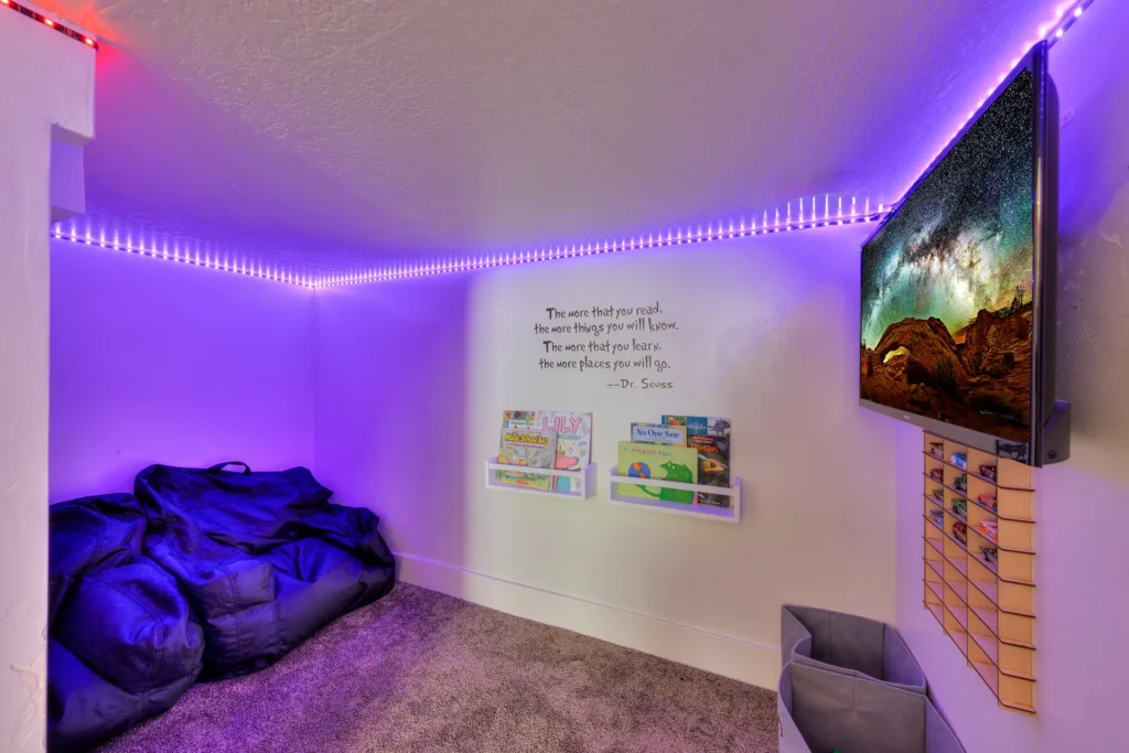 Secret children's playroom under the stairs in a Moab rental with bean bags, books, a wall-mounted TV, and LED lighting.
