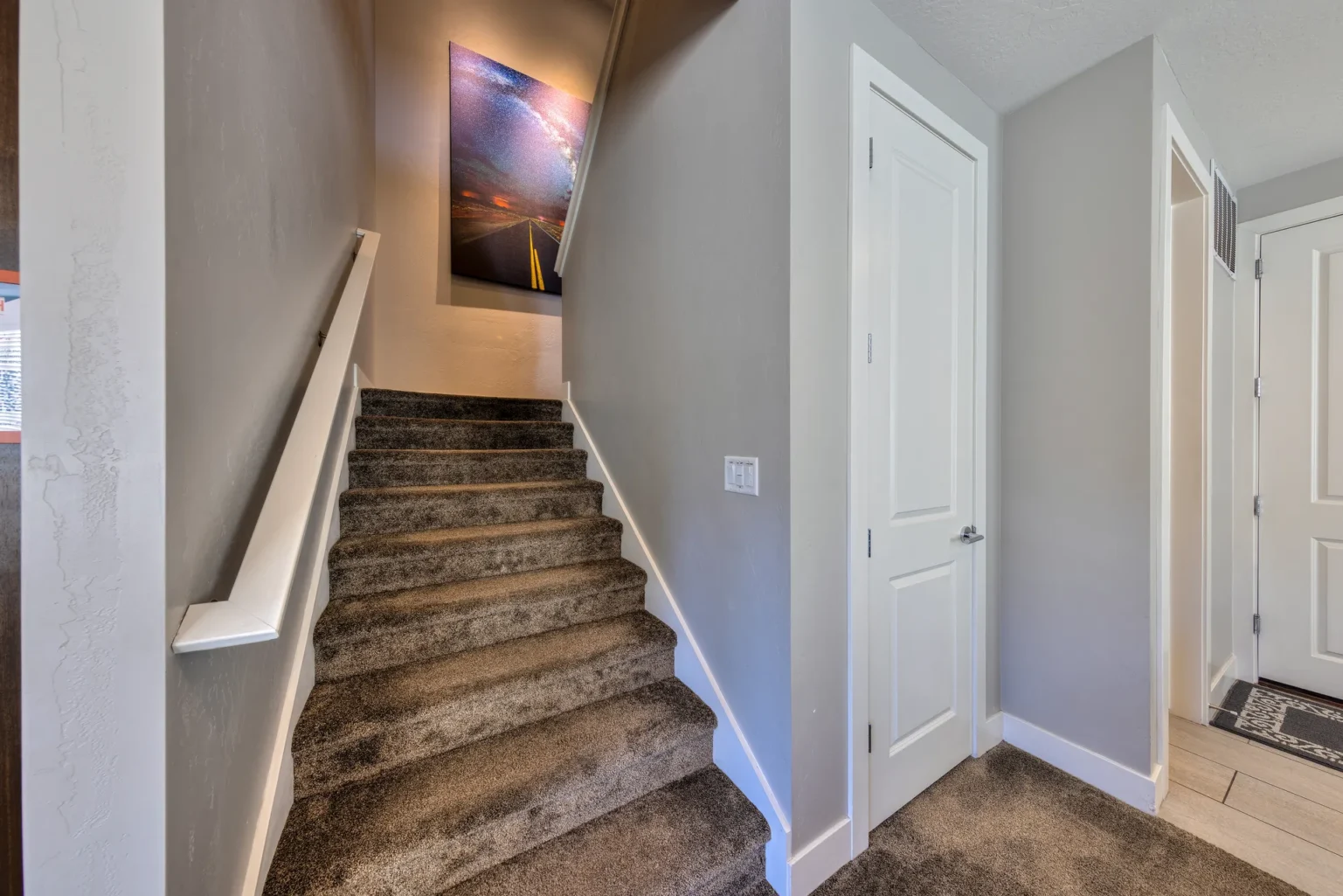029-Entrada-Moab-417-Living-Dining-Kitchen Carpeted staircase in a luxury Moab rental featuring a large Milky Way landscape photograph on the landing.