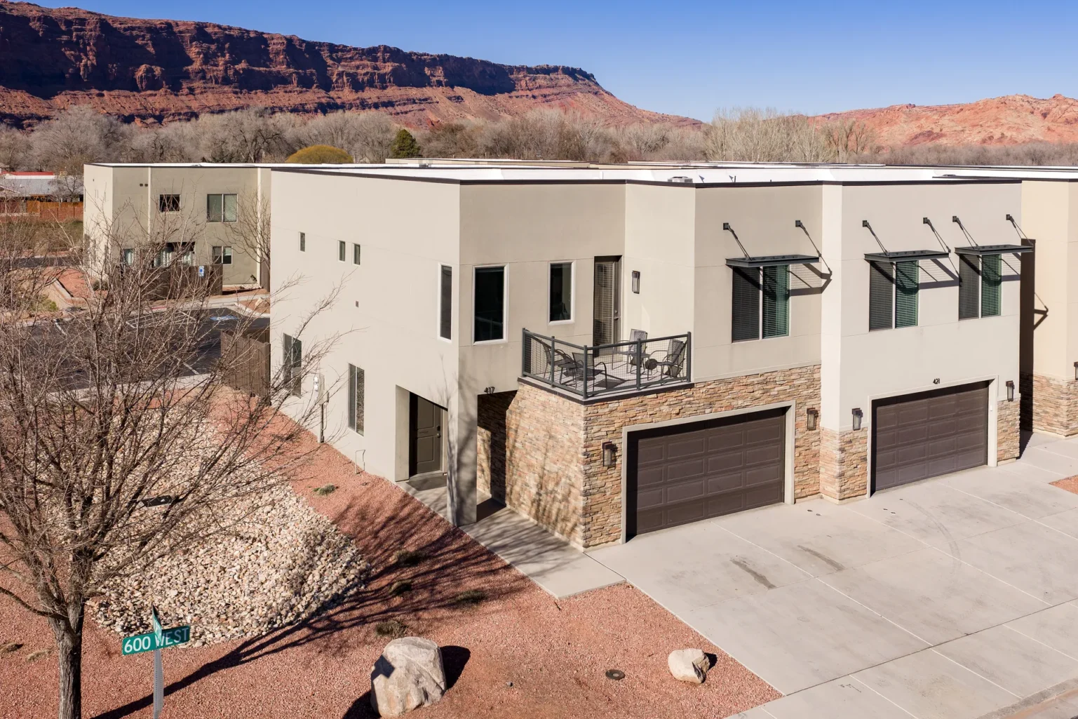 Modern beige stucco apartment building with stone base and red sandstone cliffs Aerial view of Entrada Moab townhomes featuring red rock cliffs and professional desert xeriscaping.