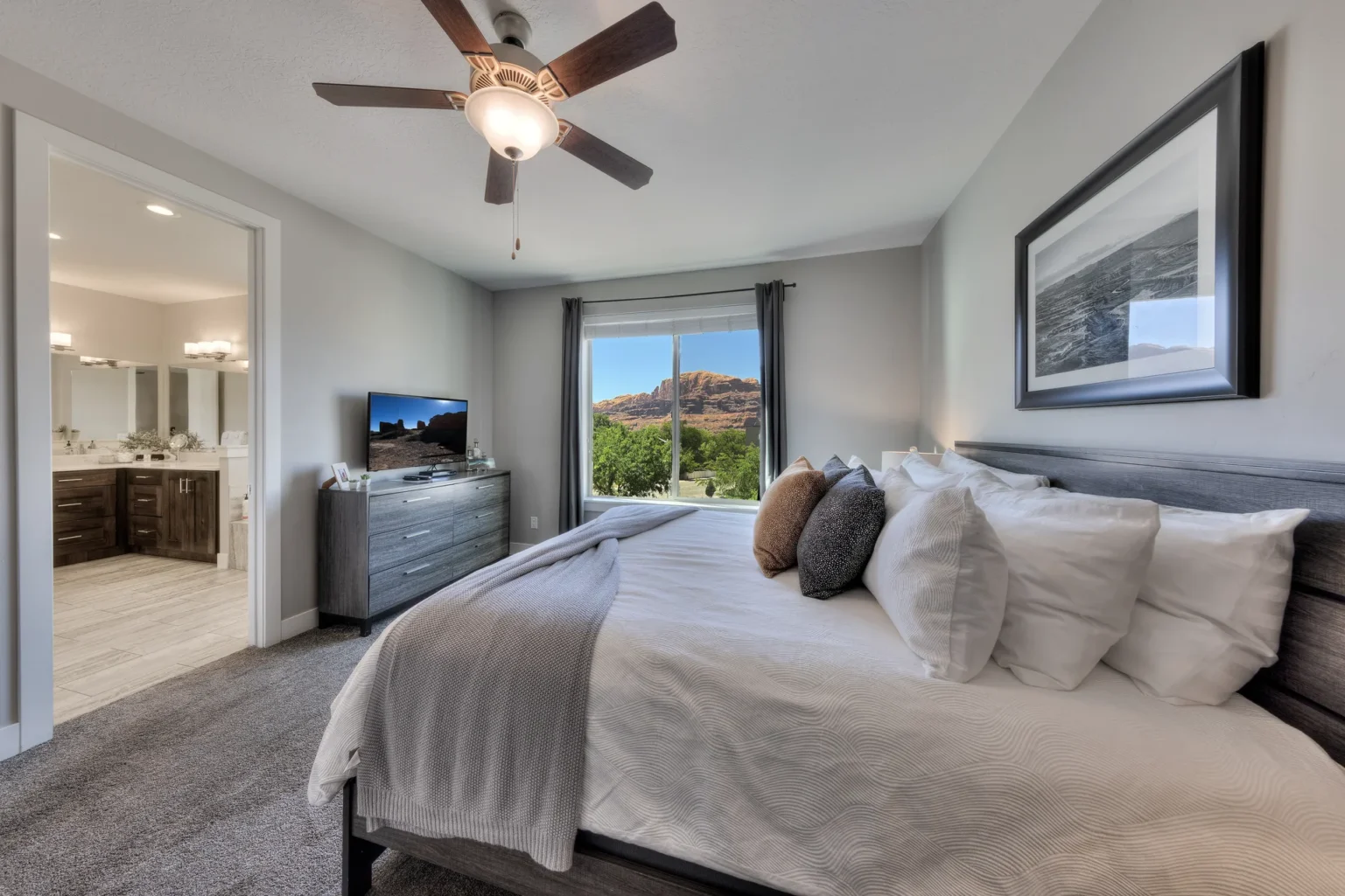 Modern gray bedroom with rocky landscape view King bed in a Moab vacation rental with a view of red rock cliffs and a wall-mounted smart TV.