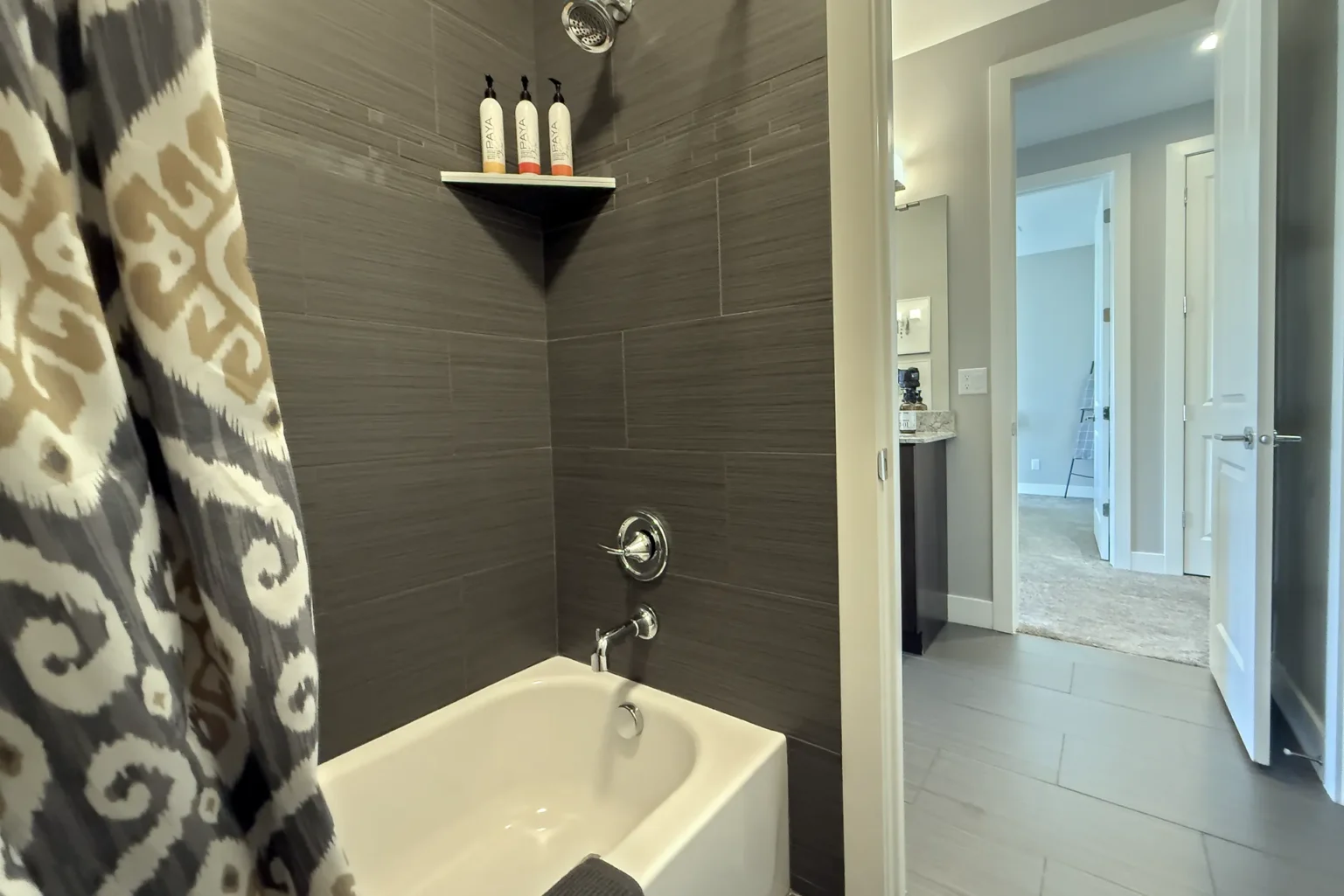 044-Entrada-Moab-417-JackAndJillBathroomWithDoubleVanity Updated tub and shower room in a Moab townhome featuring modern grey tile and Paya shampoo dispensers.